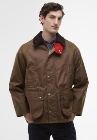 Brown waterproof jacket with a corduroy collar, red accent, snap buttons, and two front patch pockets. Textured fabric with purple trim.