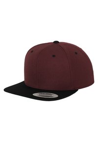 Cappellino snapback bordeaux con visiera piatta nera. Tessuto testurizzato, sei fori di ventilazione e un'etichetta circolare sul lato interno della visiera.