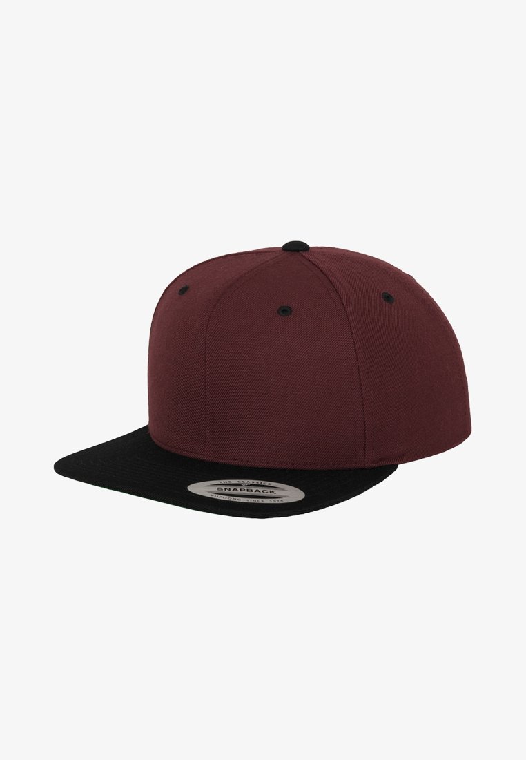 Maroon snapback cap with a black flat brim. Textured fabric, six ventilation holes, and a circular label on the underside of the brim.