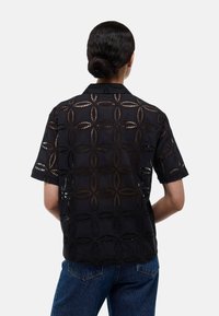 Chemise noire à manches courtes, avec des découpes en forme d'ovale, tissu texturé et un design de col classique.
