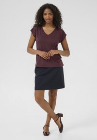 Haut bordeaux à col en V avec des manches courtes, associé à une jupe crayon navy, complété par des chaussures à talons marron. Texture de tissu lisse.