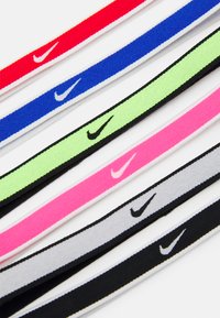 Opaski na głowę Nike w kolorach różowym, zielonym, niebieskim, czerwonym, szarym i czarnym. Miękka, teksturowana tkanina z białymi akcentami logo. Okrągły kształt; jednolita szerokość.