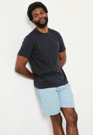 Navy-blaue Baumwoll-T-Shirt kombiniert mit hellblauen gestreiften Shorts. Das T-Shirt hat einen klassischen Rundhalsausschnitt; die Shorts verfügen über einen elastischen Bund und seitliche Taschen.