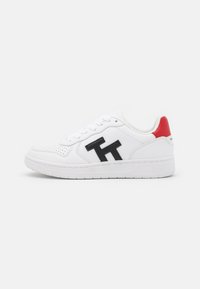 Biała skórzana tenisówka o fakturowanej powierzchni, z czarnymi akcentami logo i czerwonym detalem na pięcie. Zaprojektowana z płaską gumową podeszwą.