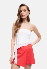 Top blanco sin tirantes con tela texturizada y dobladillo con volantes, combinado con una falda corta roja en corte A con un diseño asimétrico.