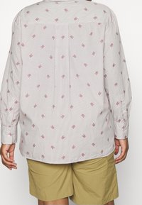 Camicia a maniche lunghe con un leggero motivo a righe, caratterizzata da piccoli rombi rossi. Tessuto testurizzato e un plissé al centro della schiena.