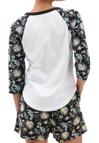 Kurzarmpyjama-Set mit einem weißen Oberteil mit schwarzen Akzenten und einer Shorts aus floralem Muster in Grüntönen, Lila und Schwarz.