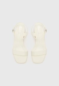 White strappy sandals with a toe and ankle strap, smooth texture, square toe design, and a subtle metallic buckle detail.