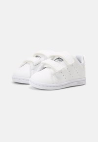 White sneakers made of synthetic material. Features Velcro straps, perforated side accents, a smooth texture, and a rubber sole.