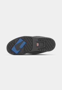 Black skate shoe sole with textured rubber, featuring a blue accent and hexagonal patterns for grip. Central logo on the heel.