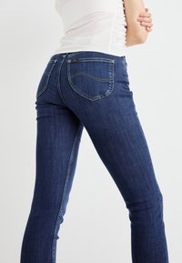 Mörkblå denimjeans med slim fit, med två bakfickor med böjda sömmar och gula sömdetaljer. Slät textur.