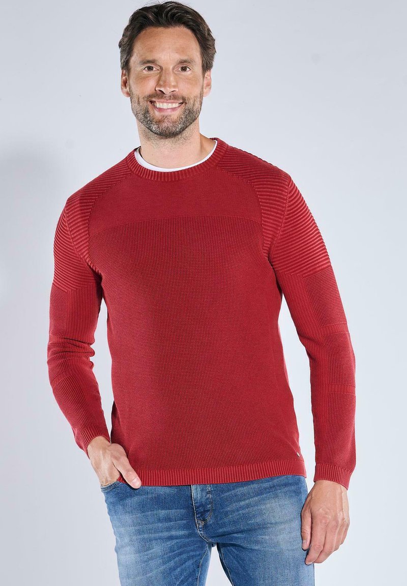Roter gestrickter Pullover mit gerippten Akzenten an den Schultern, rundem Ausschnitt und langen Ärmeln, kombiniert mit blauen Jeans. Glatte Textur.