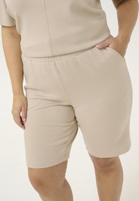Shorts beiges en tissu doux, dotés d'une taille élastique et de poches latérales, avec une coupe décontractée et une texture lisse.