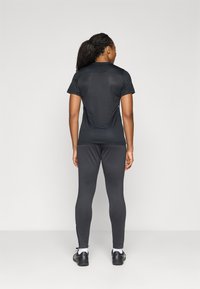 Fekete sportpóló rövid ujjakkal, sötétszürke leggingszel párosítva, amelyeken cipzárak találhatók a bokánál. Sima, jól illeszkedő anyag.