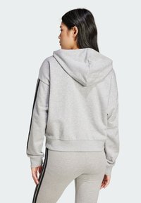 Grå hettegenser med en cropped design, som har svarte side-striper og ribbede mansjetter, laget av et mykt, teksturert stoff.