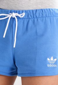 Shorts en coton bleus avec un cordon de serrage blanc et un logo Adidas brodé blanc présentant trois éléments en forme de feuille au bas.