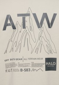 Jasny koszulka z wyraźnymi czarnymi grafikami gór, napisem "ATW" oraz tekstem związanym z sprzętem outdoorowym i treningiem.