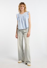 Top azzurro chiaro senza maniche con spalline arricciate e design arricciato. Abbinato a jeans grigi chiari svasati e sneakers bianche.