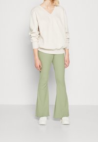 Light beige V-neck sweater with dropped shoulders paired with flared, ribbed green pants and white sneakers. Soft material, relaxed fit.