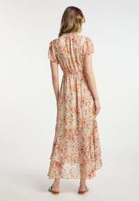 Robe longue fleurie en tissu léger, avec une taille cintrée, des manches courtes et un ourlet à volants superposés dans des tons orange et beige.