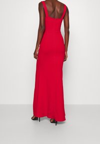 Robe maxi rouge cintrée avec larges bretelles, dos carré et fermeture éclair. Texture lisse avec un design minimaliste.