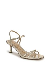 Sandal con tacco alto aperto davanti in oro metallico, con sottili cinturini, una fibbia alla caviglia e un tacco elegante e curvo. Texture liscia con una finitura lucida.