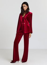 Blazer en velours rouge avec un revers en satin, fermeture à un bouton, deux poches avant, associé à un pantalon large assorti et des escarpins à bout pointu.