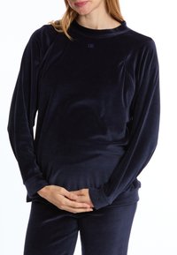 Navy blauwe fluwelen top met lange mouwen, featuring een hoge halslijn en raglanmouwen, met een zachte textuur en minimale stikseldetails.