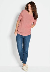 Kurze Ärmel, korallenfarbener Strickpullover mit weitem Ausschnitt, kombiniert mit blauen Jeans und hellen Sneakers. Weiche Textur, lässige Passform, minimalistisches Design.