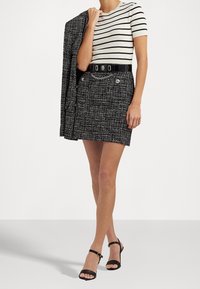 Randig kortärmad topp i svart och vitt, kombinerad med en kjol i tweed i svart och vitt, med ett bälte som har kedjedetaljer och en knappaccent.