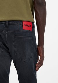 Tummansiniset farkut, joissa punainen HUGO-logotarra takataskussa. Kangas on hieman karkeaa ja leikkaus on istuva.