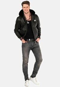 Zwarte gewatteerde leren jas met een bontkraag, zwart shirt, grijze skinny jeans en witte sneakers. Accessoires omvatten armbanden en een ketting.