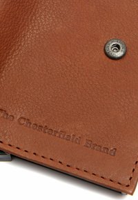 Portafoglio in pelle marrone con superficie testurizzata, caratterizzato da un marchio in rilievo e un dettaglio con bottone a pressione metallico. I bordi cuciti sono visibili.