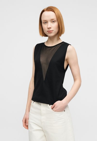 Haut noir sans manches avec un devant transparent en forme de V et un dos uni, doté d'un col rond et d'une coupe décontractée, associé à un pantalon de couleur crème.