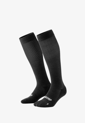 Calze a compressione alte fino al ginocchio in nero uniforme con texture a costine, caratterizzate da punta e tallone rinforzati. Logo CEP stampato sulla suola.
