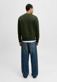 Mørkegrønt sweatshirt med rund hals, parret med løstsiddende blå denimjeans med baglommer og en gradvis falmning.