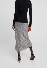 Haut noir à manches longues assorti d'une jupe mi-longue à motif tacheté noir et blanc, porté avec des chaussures noires à talons hauts.