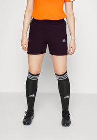 Schwarze Sportshorts mit enger Passform und Seitentaschen, kombiniert mit knielangen schwarzen Socken mit weißen Streifen und Logos.