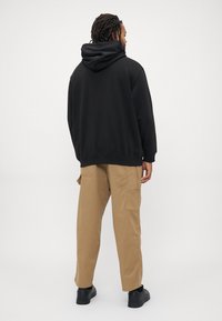 Black hooded sweatshirt with a relaxed fit, paired with khaki cargo pants featuring side pockets and ankle-length cut, worn with black shoes.