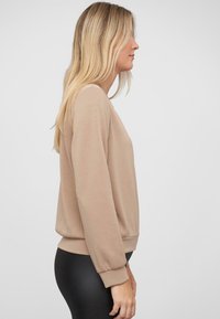 Beige sweatshirt met lange mouwen, geribbelde manchetten en zoom. Zachte textuur en een relaxte pasvorm, gecombineerd met zwarte leggings.