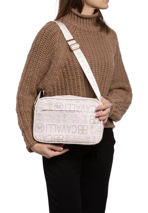 Borsa a tracolla beige con motivo del logo in rilievo, caratterizzata da una texture liscia e tracolla regolabile, tenuta da una persona che indossa un maglione lavorato a maglia.
