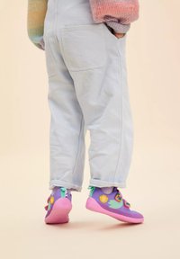 Lila- und rosa Schuhe mit einer strukturierten Oberfläche, die farbenfrohe Akzente aufweisen, kombiniert mit hellblauen Stretch-Stoff-Hosen mit umgeschlagenem Saum.