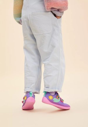Lila- und rosa Schuhe mit einer strukturierten Oberfläche, die farbenfrohe Akzente aufweisen, kombiniert mit hellblauen Stretch-Stoff-Hosen mit umgeschlagenem Saum.
