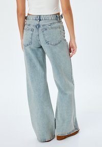 Jeans de mezclilla de tiro alto, de pernera ancha y color azul claro, con dos bolsillos traseros y una textura ligeramente desgastada.