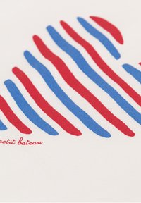 Katoenen stof met rode en blauwe golvende strepen op een witte achtergrond, met "Petit Bateau" in het rood gedrukt aan de onderkant.