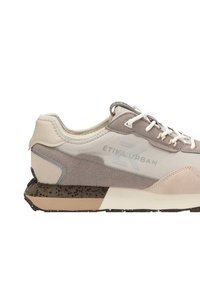 Zapatillas que combinan materiales en tonos beige y gris, con texturas de cuero liso y ante, cordones blancos y una suela moteada con acentos marrones.