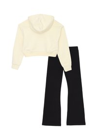 Felpa corta color crema con tasca frontale e leggings neri svasati, entrambi realizzati in tessuto morbido, caratterizzati da una superficie liscia e senza motivi visibili.