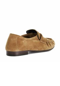 Tan suede moccasin with a rounded toe, decorative bow detail, and a low wooden heel. Soft texture and minimalist design elements.