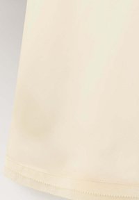 Gros plan de l'ourlet sur un vêtement en tissu beige clair avec une double couture et un détail de bord festonné.
