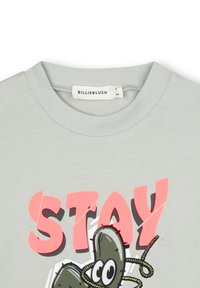 T-shirt in cotone grigio chiaro con grafica audace in rosa che recita "STAY" e un design di cartone di un cactus con contorni neri e accenti verdi.